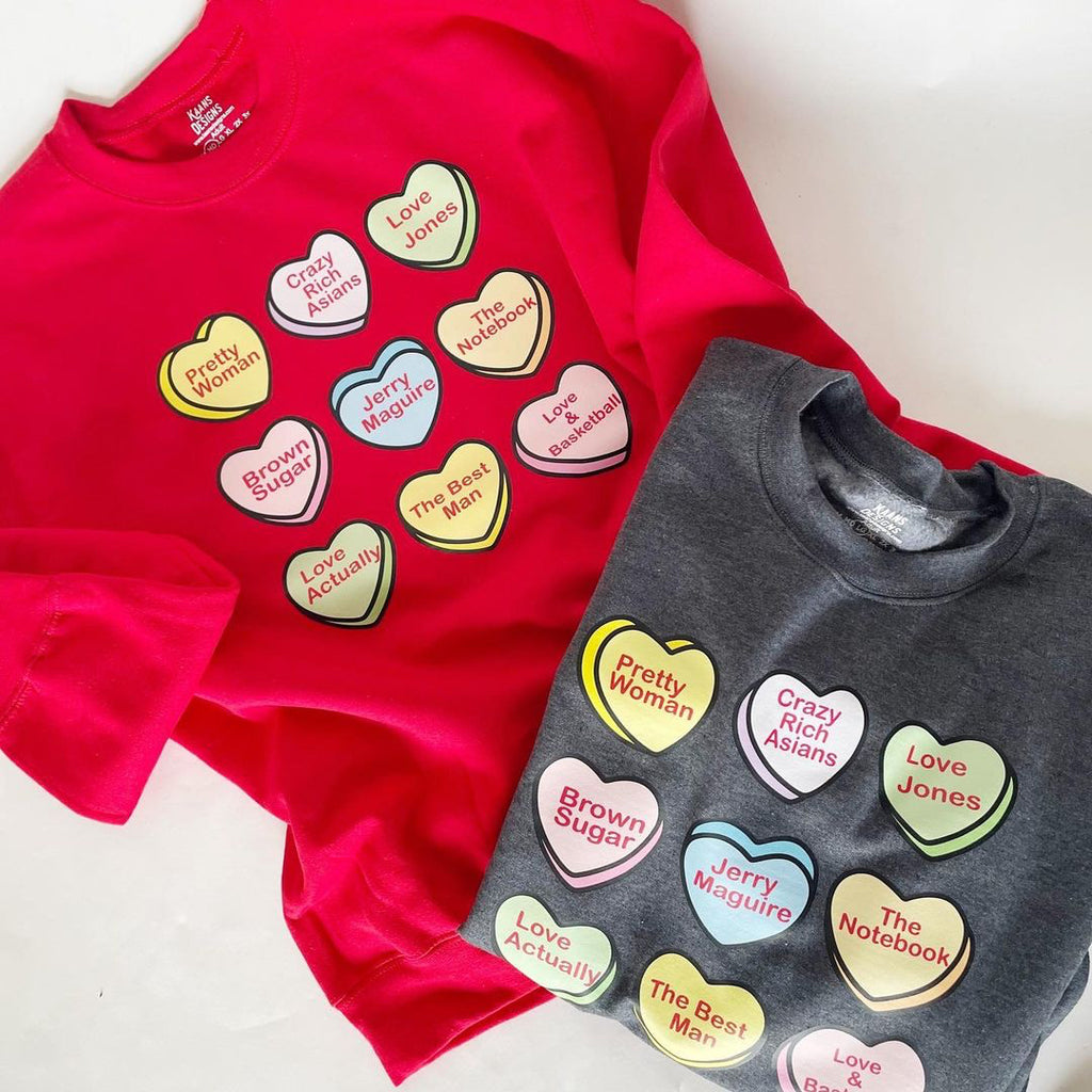 red shirt with valentines day theme candy hearts that are different colors with romantic or love movies listed, there is a charcoal grey color sweatshirt option also