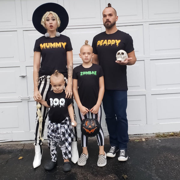 Family of 5, mom and a dad dressed in matching halloween graphic shirts in front of garage ready for trick or treat. Like Modern Day Adams Family. Mom Shirt says Mummy, Dad is Deaddy, Kid is Zombae, and Toddler is Boo
