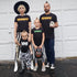 Family of 5, mom and a dad dressed in matching halloween graphic shirts in front of garage ready for trick or treat. Like Modern Day Adams Family. Mom Shirt says Mummy, Dad is Deaddy, Kid is Zombae, and Toddler is Boo