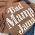 close up of a flat lay of a brown hoodie with cream ink screen print design that says bad mama jama, laying on some cute everyday blue jeans for a cozy outfit for moms with a cute saying. hoodie color also called pecan