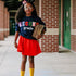 little girl in navy custom sweatshirt with chenille patches that are multi colored in a red skirt, black girl magic representing education holding books in yellow socks
