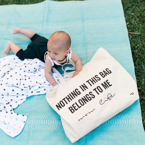 baby getting tummy time at the park on the grass and blanket next to mom tote bag, nothing in this bag belongs to me canvas tote bag with graphic text