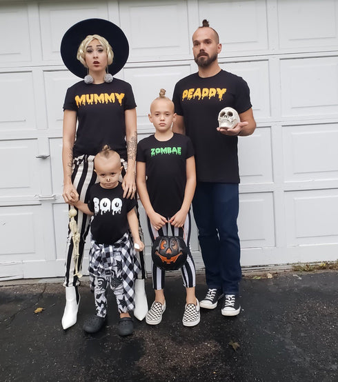 family matching in halloween shirts creating cute costume for hallowen night, reminds you of the adams family in modern day screen print design tshirts are mummy deaddy boo zombae holding a pumpkin bag for candy mom in a witch hat and dad holding a skull