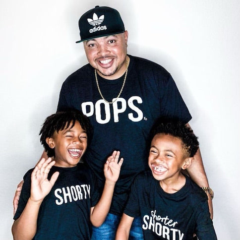 black dad and his two sons matching in screen print designs that say pops shorty and shorter shorty for a fathers day photo shoot